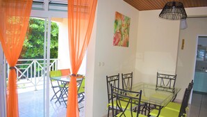 Een eetgedeelte met een glazen tafel en stoelen, oranje gordijnen en een schilderij aan de muur.