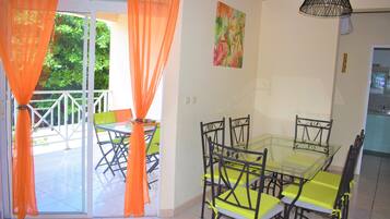 Un coin repas avec une table et des chaises en verre, des rideaux orange et un tableau accroché au mur.