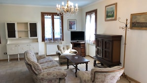 A living room with floral armchairs, a wooden coffee table, a TV, and a chandelier. - Bright country villa, with veranda, pool, garden, near Florence (Buggiano)