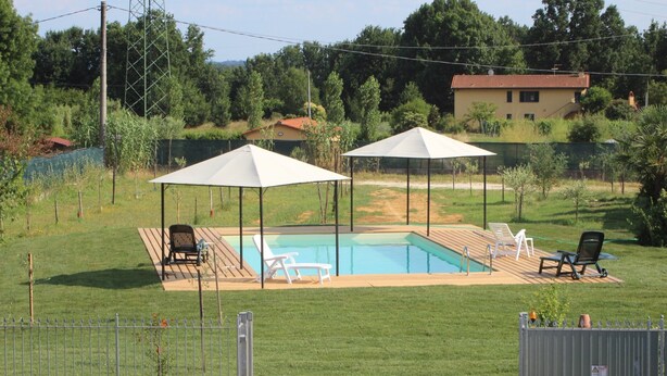A swimming pool with two white canopies, surrounded by a fenced area with a grassy lawn and a few lounge chairs. - Bright country villa, with veranda, pool, garden, near Florence (Buggiano)