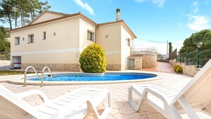 Ein Haus mit Swimmingpool, weißen Liegestühlen und einer Steinmauer.