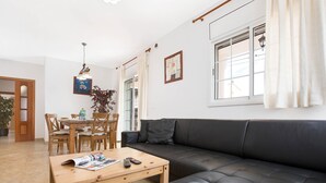 Ein Wohnzimmer mit einer Couch, einem Couchtisch, einem Esstisch, Stühlen und einer Zimmerpflanze.