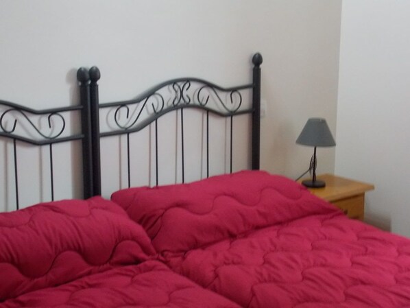 Una cama con cabecera de metal negro y una manta roja.
