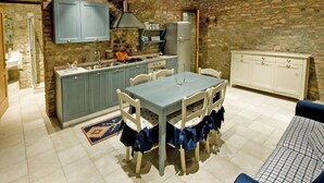 A rustic kitchen with stone walls, a blue cabinet, a white refrigerator, and a dining table with chairs. - Apartment in a nineteenth-century house                                        (Cervarese Santa Croce)