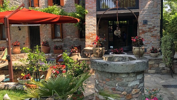A courtyard with a stone fountain, potted plants, and a red umbrella. - Apartment in a nineteenth-century house                                        (Cervarese Santa Croce)