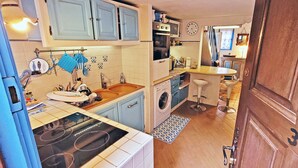 Cocina compacta con estufa, lavaplatos y lavadora. Hay armarios azules, un reloj y una pequeña barra.