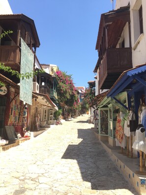 Une ruelle étroite pavée, bordée de bâtiments traditionnels, dont certains sont dotés de balcons et d’échoppes au rez-de-chaussée.