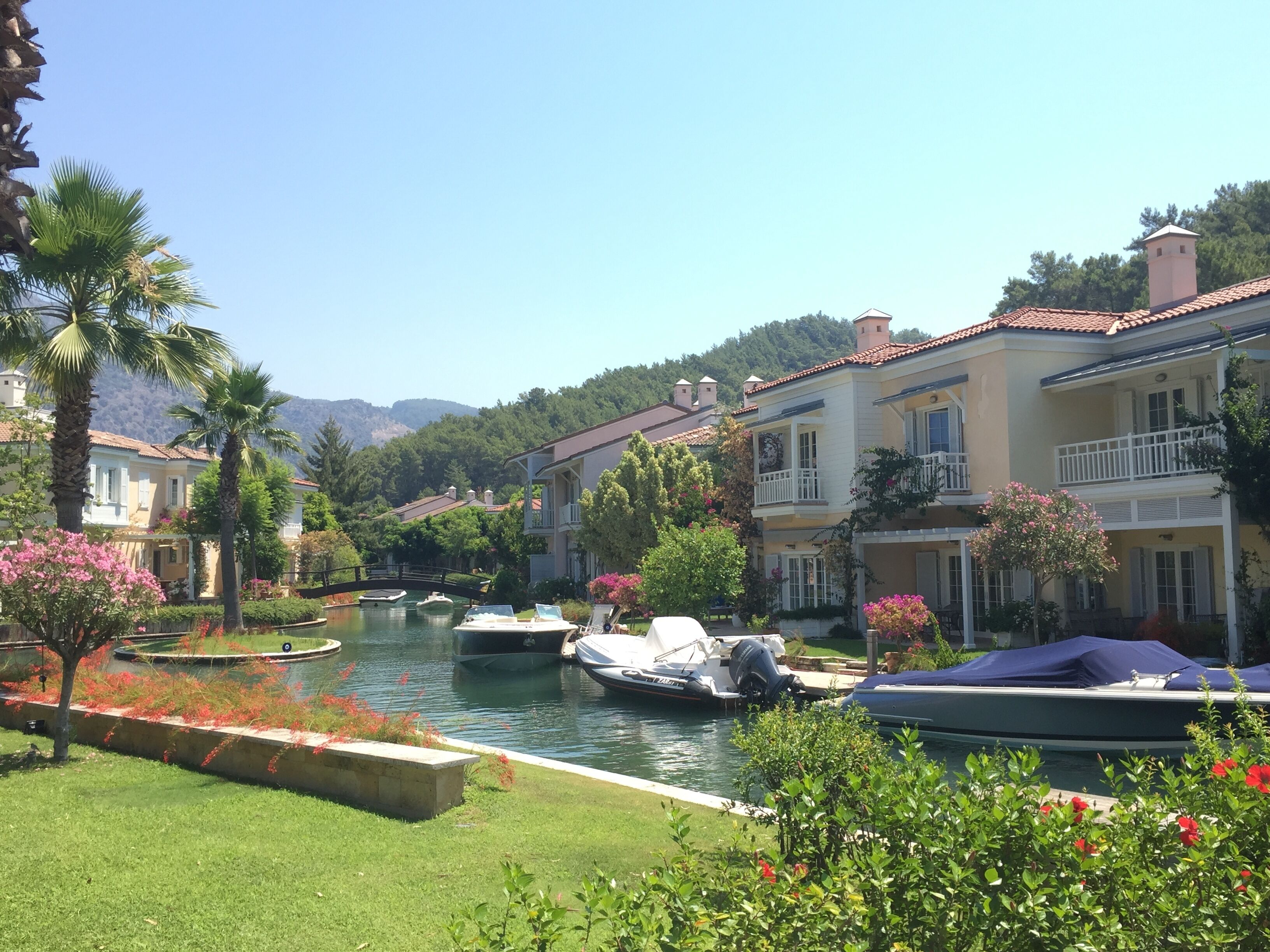 A canal with boats, surrounded by lush greenery and traditional buildings with balconies.