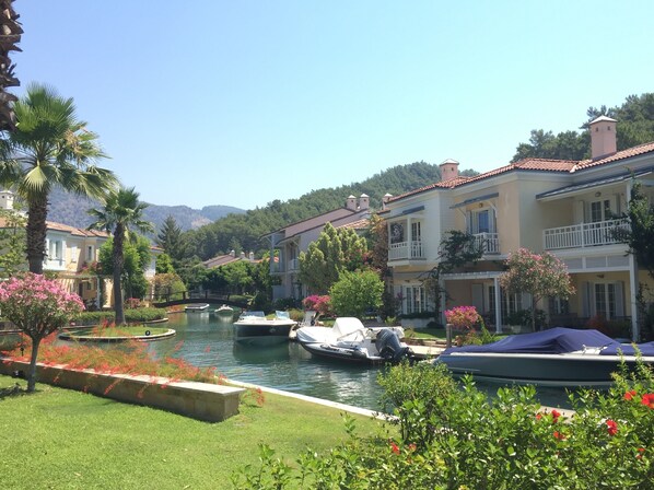 A canal with boats, surrounded by lush greenery and traditional buildings with balconies.
