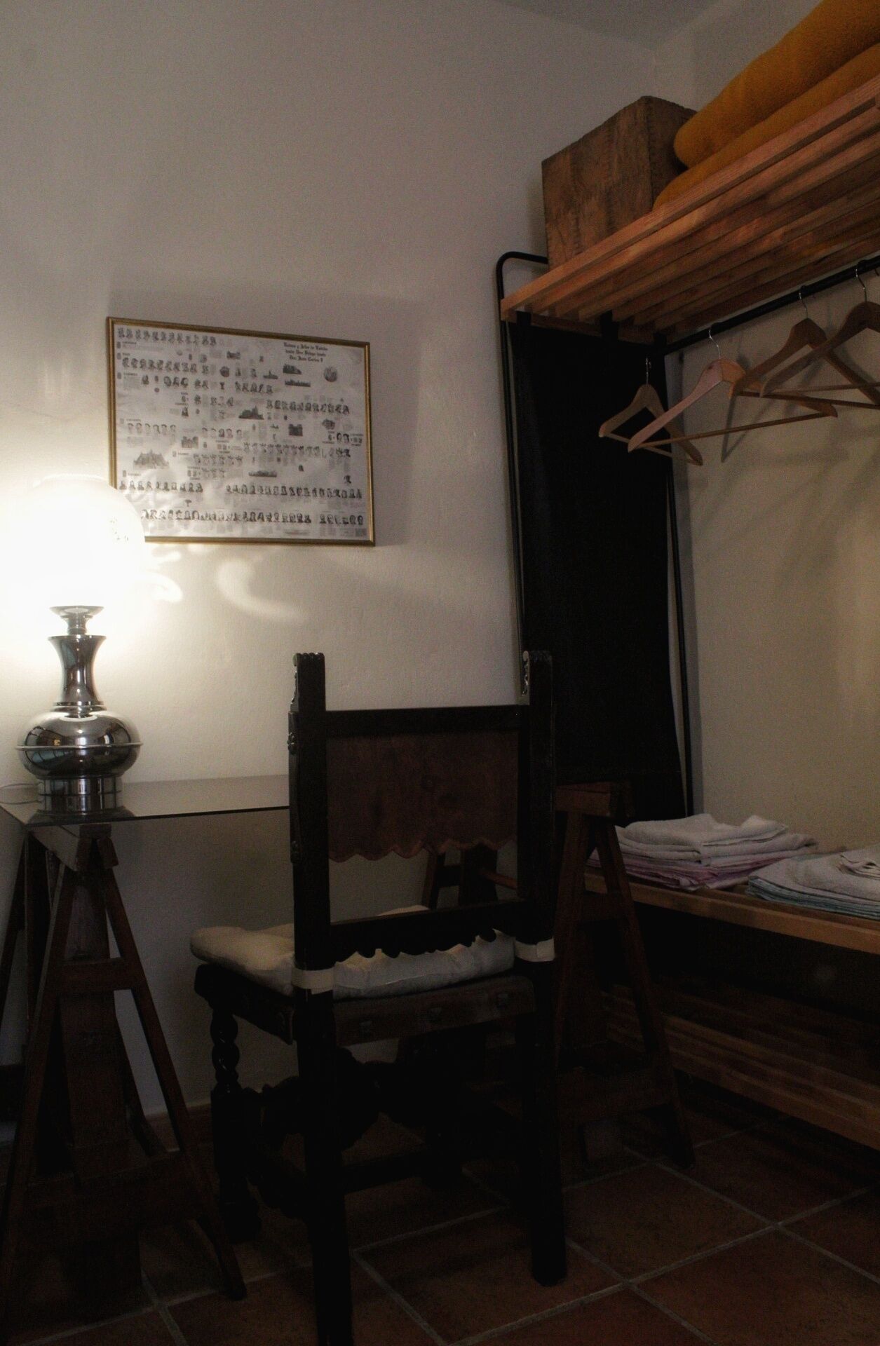 Une pièce comprenant une chaise en bois, une petite table avec une lampe et un porte-manteau fixé au mur.