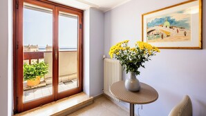 Quarto com porta de vidro deslizante para uma varanda, uma mesa redonda com um vaso de flores amarelas e um quadro na parede.