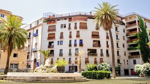 Um edifício com vários andares, varandas, uma fonte central e palmeiras.