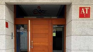 Una entrada de edificio con puerta de madera, un cartel con las letras "AT" encima, y un pequeño letrero en la puerta que indica "Apartamentos La".