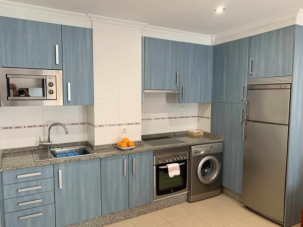 A modern kitchen with blue cabinets, a stainless steel microwave, a sink, a built-in oven, and a washing machine.