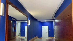 Un pasillo con paredes azules, piso de mármol y una puerta blanca.