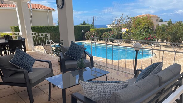 Eine Terrasse mit Gartenmöbeln, einem Pool und Meerblick.