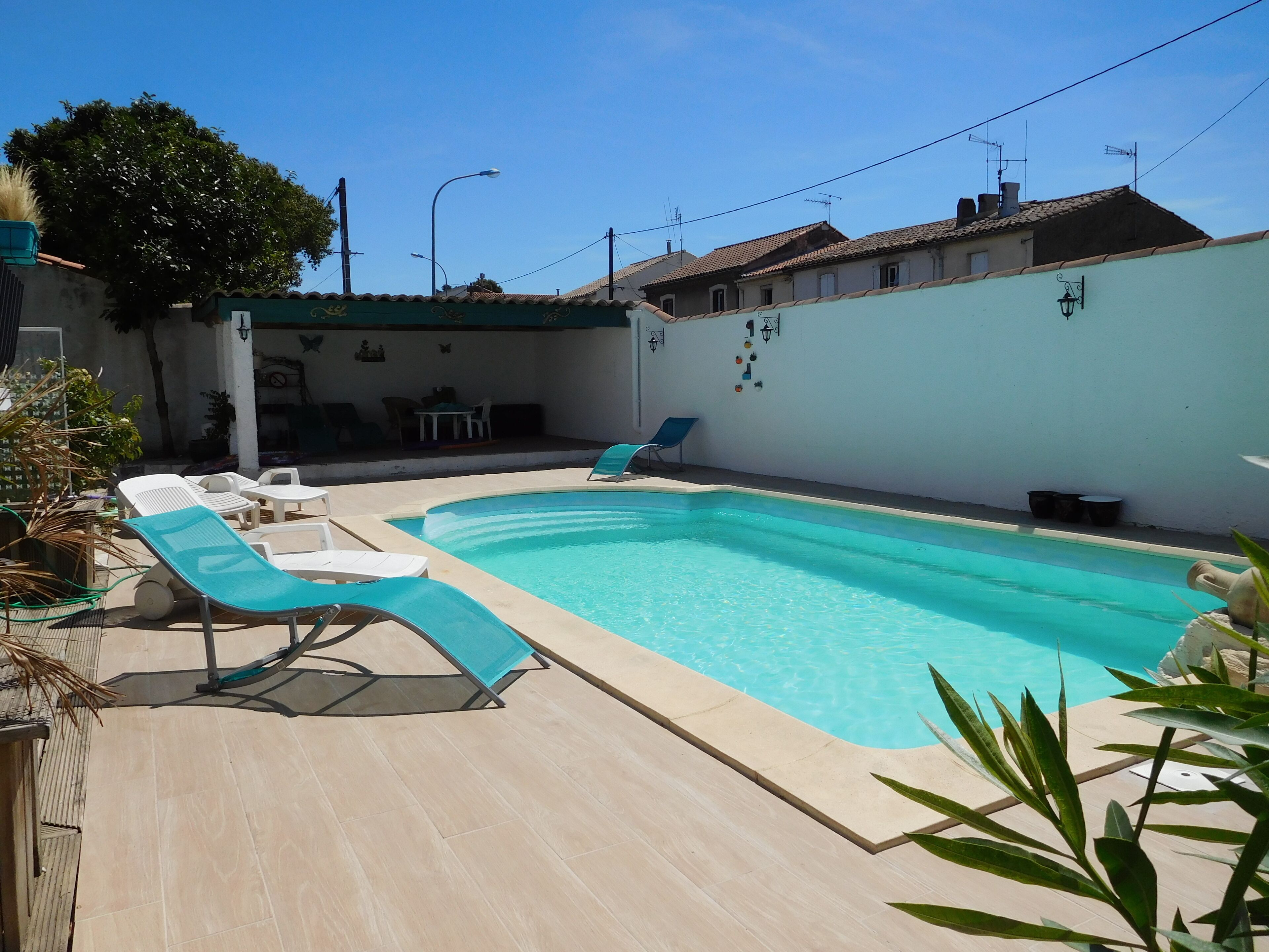 Une piscine rectangulaire avec une terrasse carrelée, entourée de chaises longues et d’une petite table.