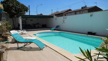 Une piscine rectangulaire avec une terrasse carrelée, entourée de chaises longues et d’une petite table.