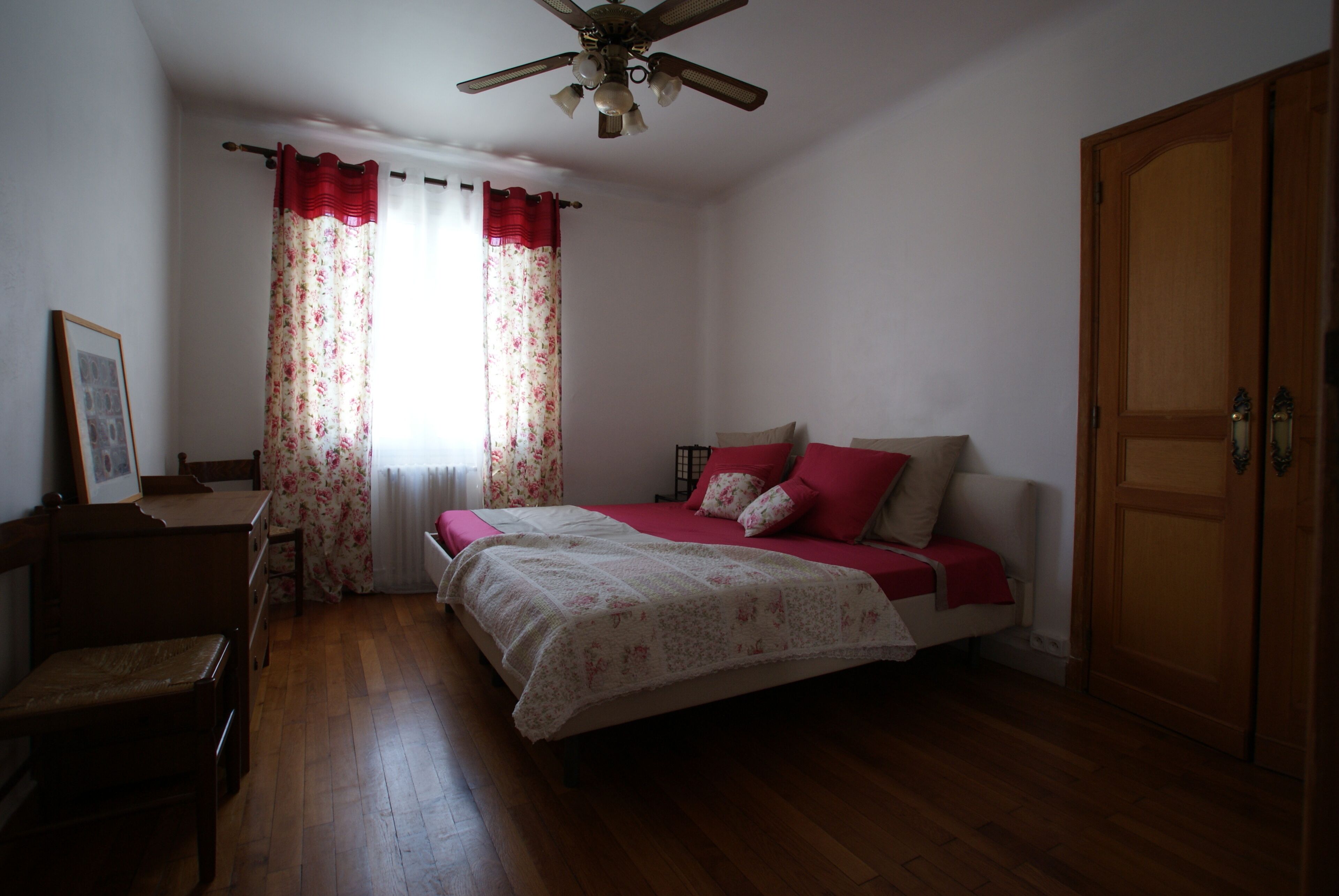 A bedroom with a bed, a wooden wardrobe, a desk, and a chair.
