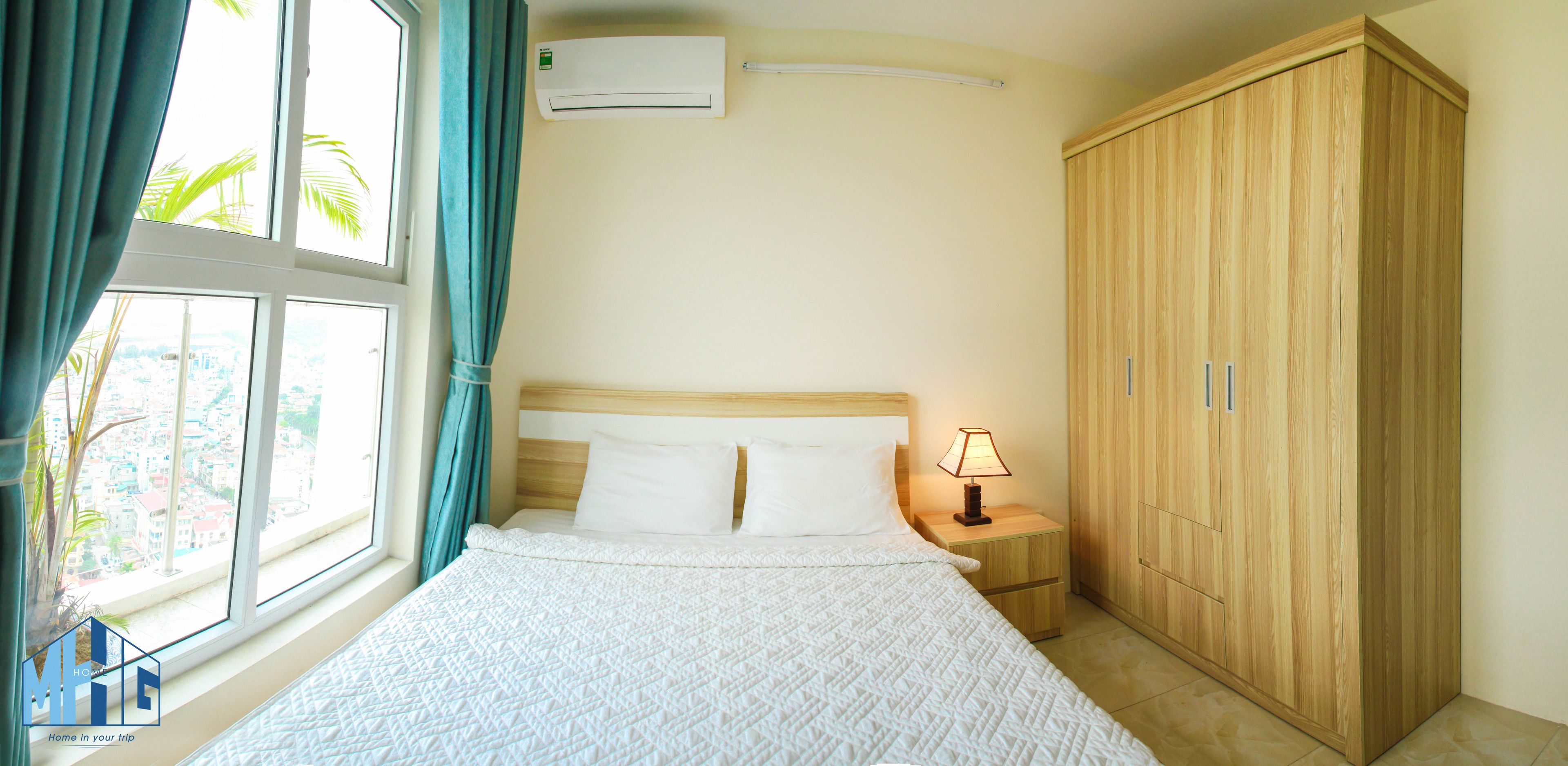 A hotel room with a bed, a nightstand with a lamp, a wardrobe, and a window with curtains.