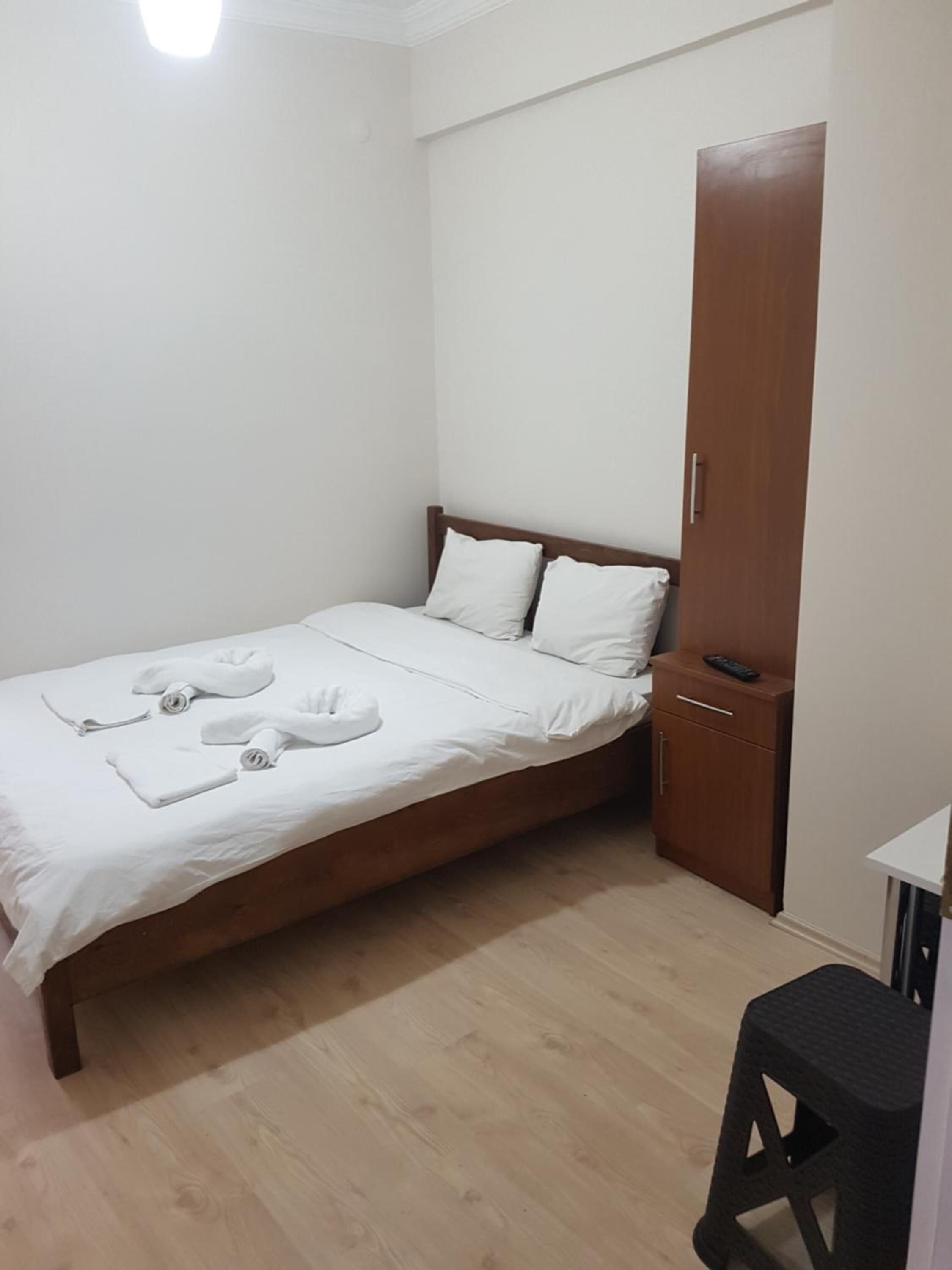 Un letto piccolo e ordinato con lenzuola e asciugamani bianchi, un armadio in legno e uno sgabello.