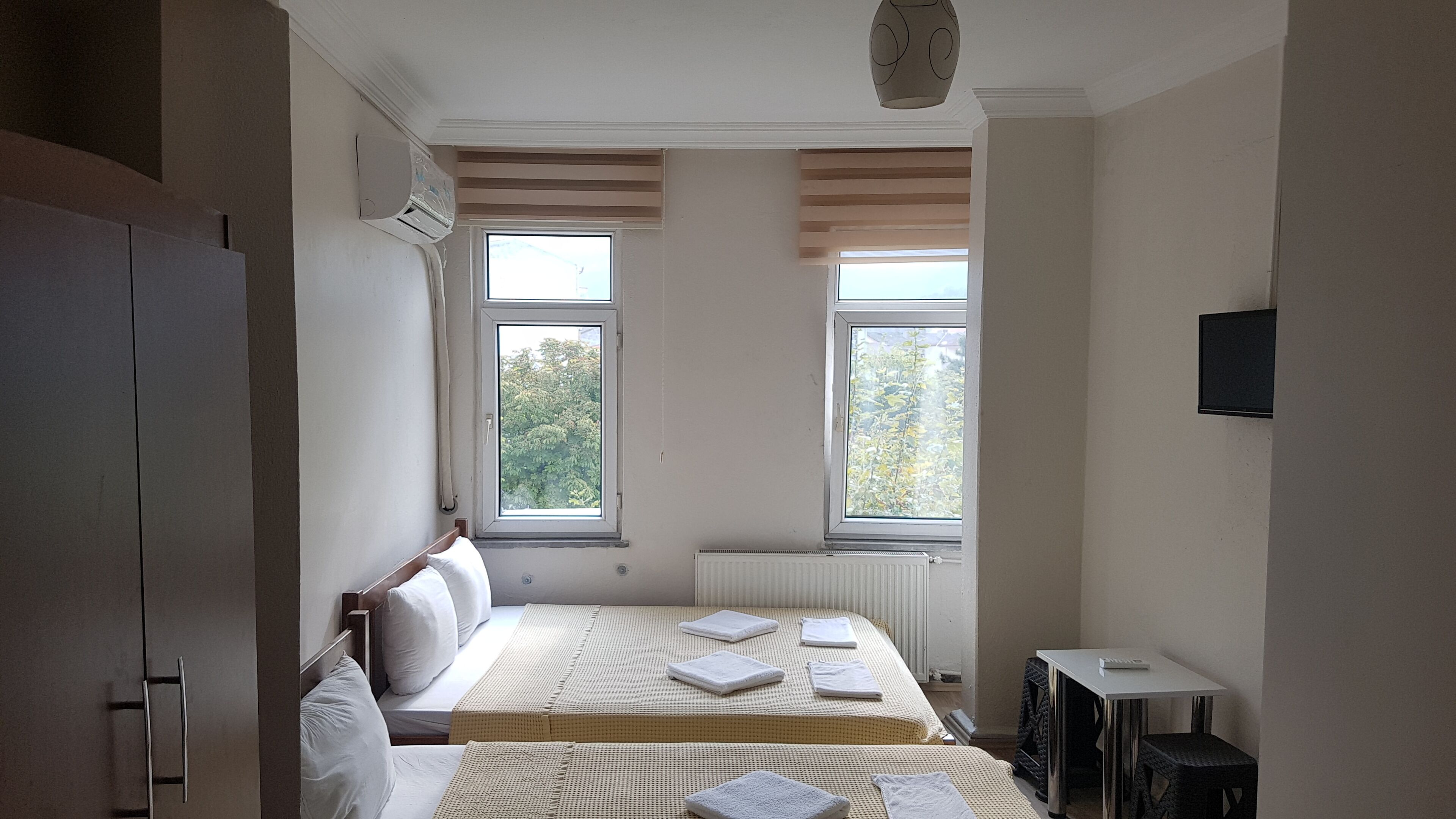 A bedroom with a bed, a radiator, two windows, a TV, and a wardrobe.