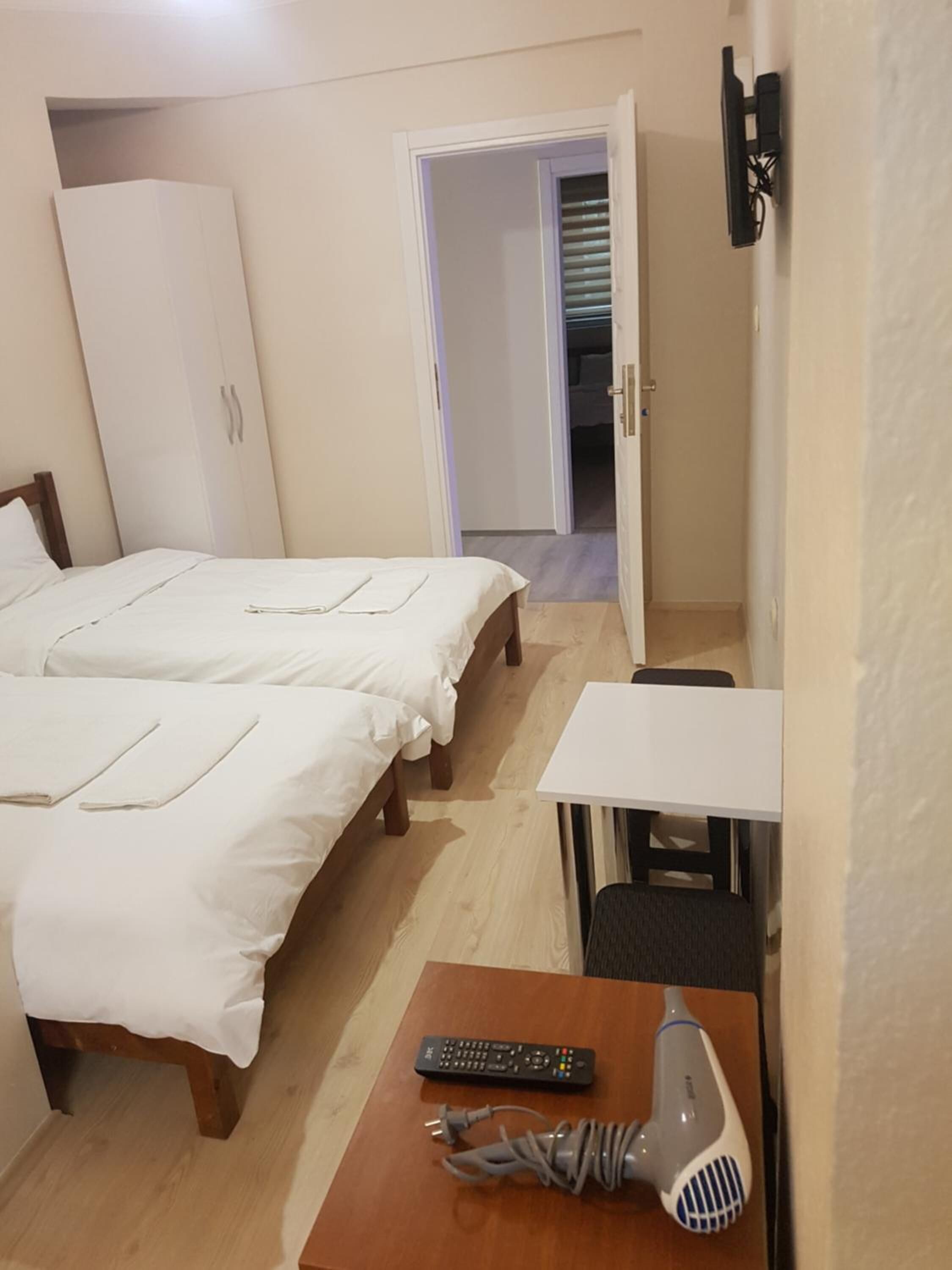 Una habitación pequeña y ordenada con dos camas, un escritorio, una silla, un secador de pelo y un control remoto.