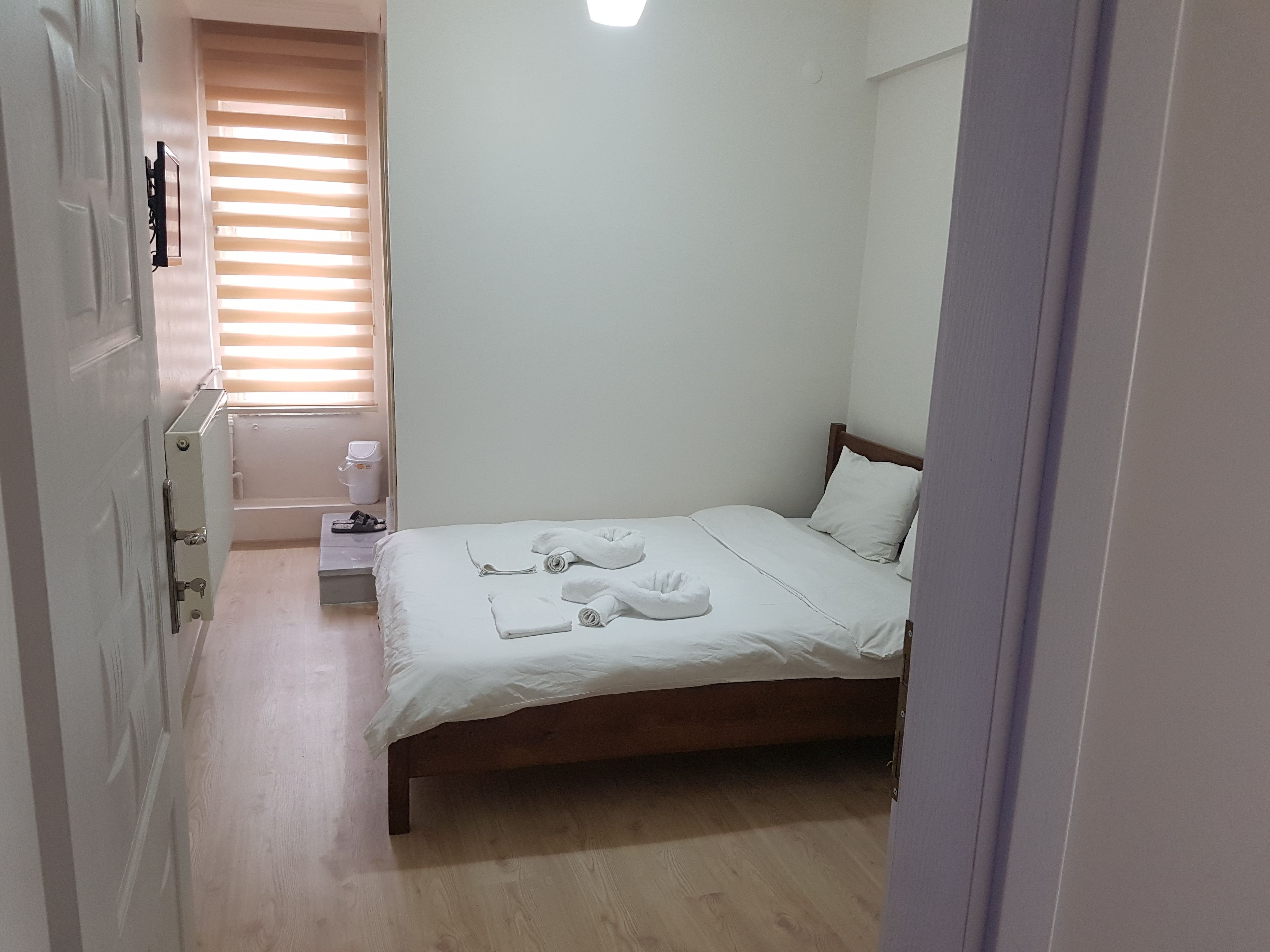 Une chambre à coucher avec un lit en bois, du linge de lit blanc, une petite table de chevet et une fenêtre avec des stores.
