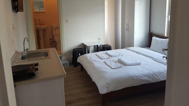 A hotel room with a bed, a sink, a mirror, a wardrobe, and a small stool. - Hakbilir Pansiyon (Amasra)