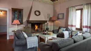 A cozy living room with a fireplace, two sofas, a table with drinks, and a window with curtains. - Tregole (Castellina in Chianti)