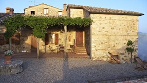 A stone building with a covered patio, outdoor seating, and a small garden area. - Tregole (Castellina in Chianti)