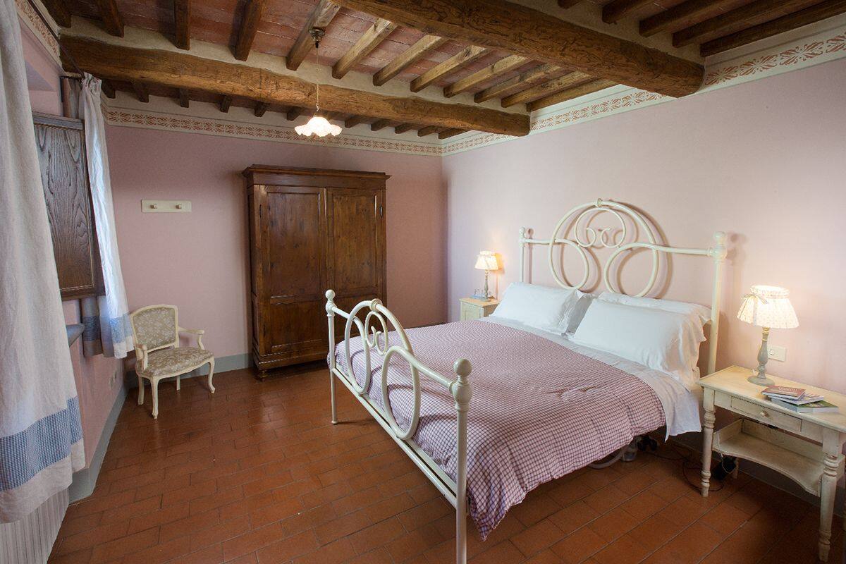 A bedroom with a bed, a wooden wardrobe, a chair, and a nightstand with a lamp.