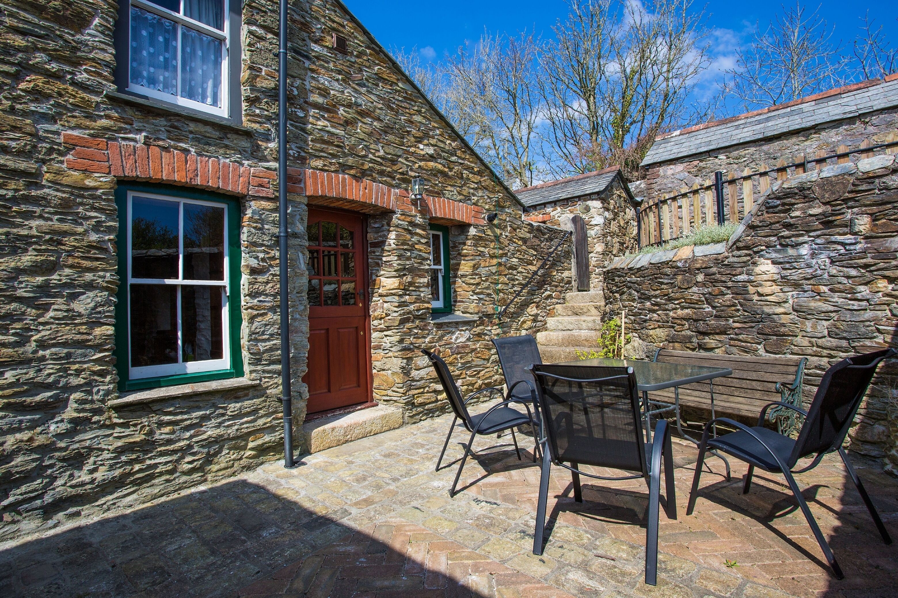 A stone building with a wooden door, a window with green trim, and a patio with outdoor furniture.