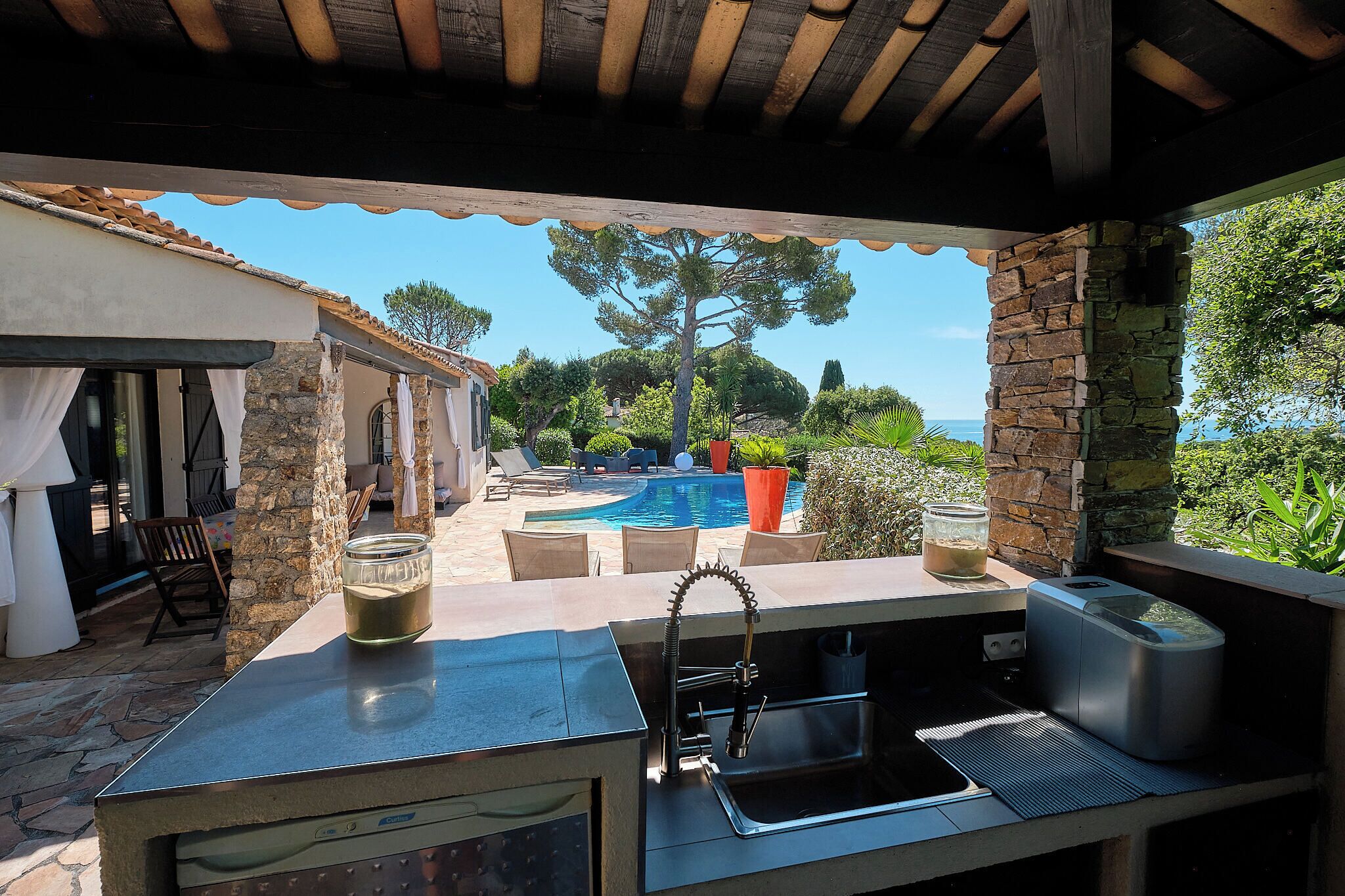 Un espace cuisine extérieur avec un mur en pierre, une piscine et une vue sur la mer.