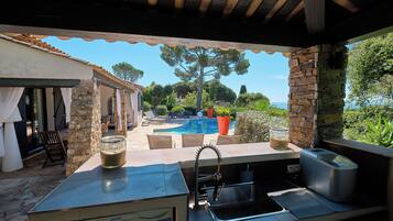 Un espace cuisine extérieur avec un mur en pierre, une piscine et une vue sur la mer.