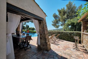 Une terrasse extérieure avec une table en pierre, des chaises et une vue sur une piscine.
