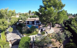 Une villa dotée d’une piscine, entourée d’une végétation luxuriante et de chemins en pierre.