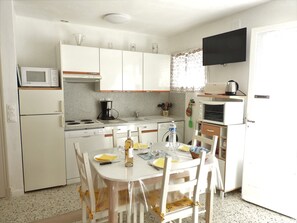 Eine kompakte Küche mit weißen Geräten, einem Esstisch mit Stühlen und einem an der Wand montierten Fernseher.