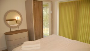 A bedroom with a bed, a bedside table, a mirror, and a window with yellow blinds.