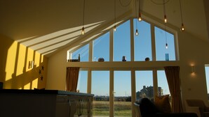 A room with large windows, a kitchen area, and a view of the outside.