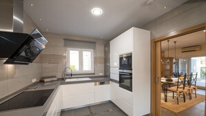 A modern kitchen with a built-in oven, a dishwasher, and a large window providing natural light. - Modern villa with HEATED POOL & 400 m from the spa La Laguna hotel (Quesada, Alicante)