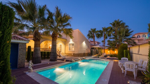 A swimming pool with a wooden deck, surrounded by palm trees and a building with a tiled roof. - Modern villa with HEATED POOL & 400 m from the spa La Laguna hotel (Quesada, Alicante)