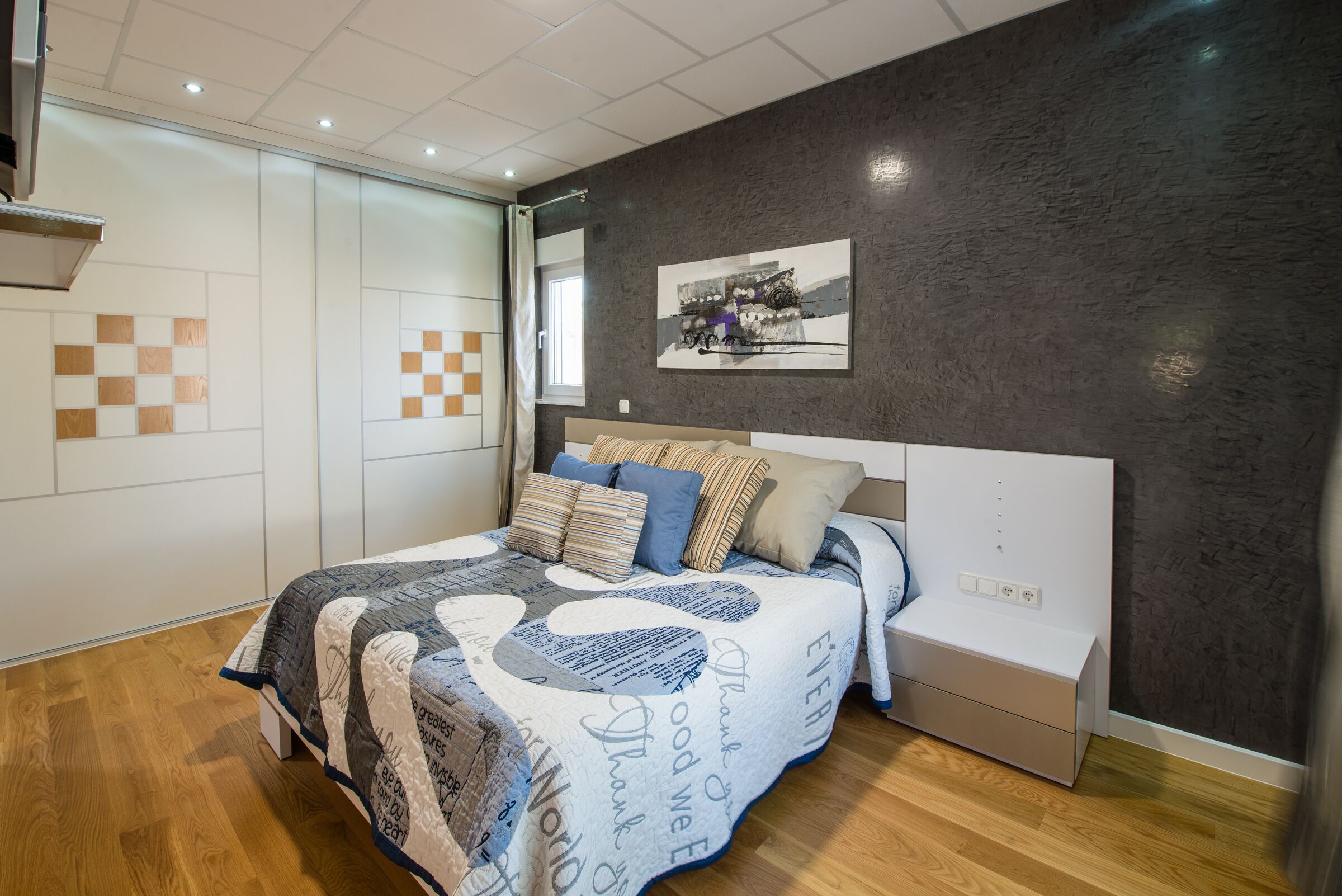 Ein modernes Schlafzimmer mit einem großen Bett, einem Nachttisch, einem an der Wand befestigten Kunstwerk und einem Karomuster an der Wand.