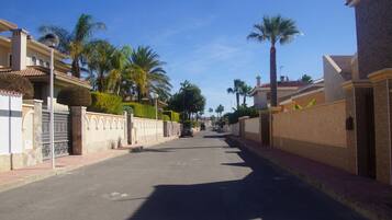 A residential street with houses, palm trees, and a clear blue sky.