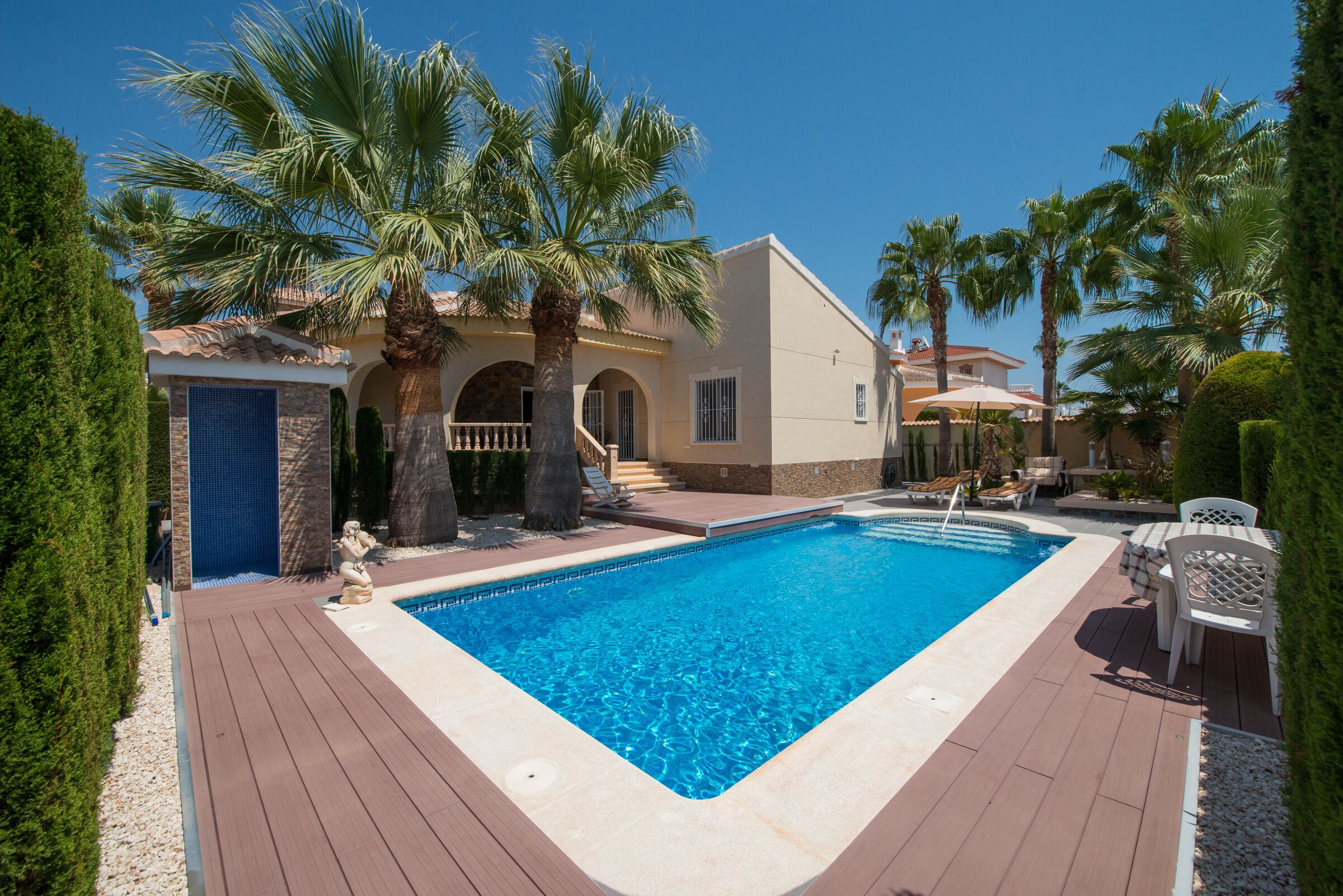 Una piscina con muelle de madera, palmeras y un edificio con techo de tejas.