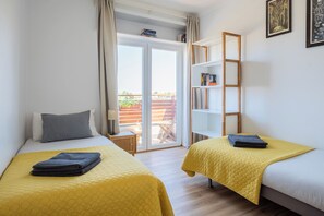 Relax in this stylish room with two single beds, a bookshelf, and a sliding door leading to an outdoor area with city views.