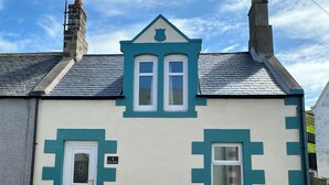 A two-story building with a white and teal facade, a small dormer window, and a chimney.