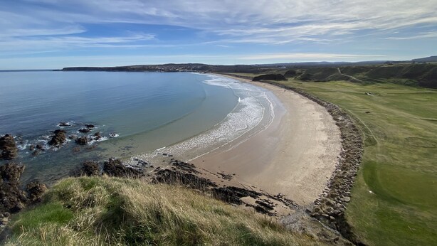 A coastal landscape with a sandy beach, grassy areas, and a clear sky.