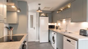 A modern kitchen with grey cabinets, a built-in oven, a microwave, a washing machine, and a dishwasher.