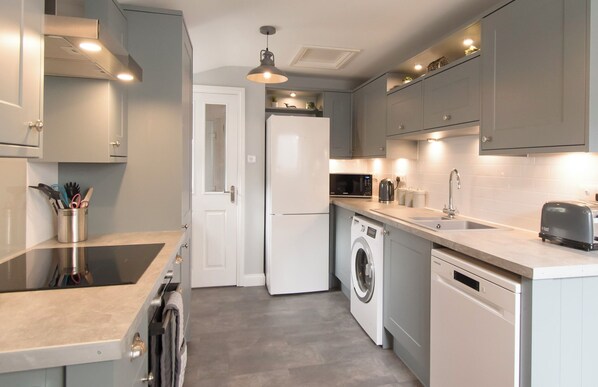 A modern kitchen with grey cabinets, a built-in oven, a microwave, a washing machine, and a dishwasher.